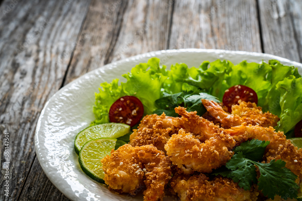 Wall mural Fried panko prawns with lime, tomatoes and greens wooden table
