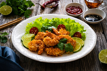 Fried panko prawns with lime, tomatoes and greens wooden table
