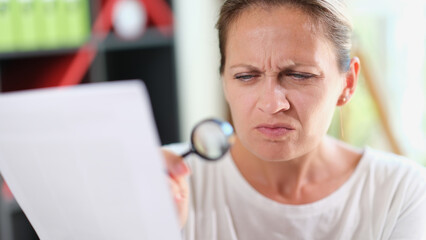 Woman with puzzled face reads document or recipe with magnifying glass in her hand.