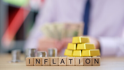 Word inflation collected from cubes and blurred coins, gold and businessman counting money in background.