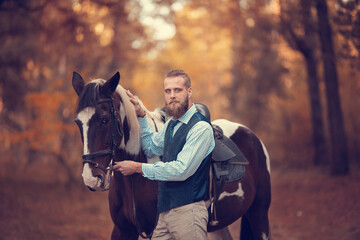 Handsome young man with a blond beard, possibly a groom at a wedding, on an autumn walk with a horse