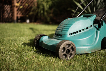 Mowing the lawn in the garden with an electric mower. Electric mower made of green plastic, designed for home gardens, standing on the grass. Well-kept garden. Blurred background.