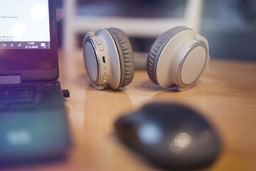 Wireless headphones lying on the table next to a laptop and a mouse.