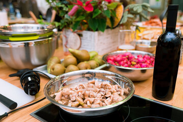 a set of ingredients on the kitchen table: a bowl of mushrooms, fresh pears and a bottle of wine, kitchen utensils