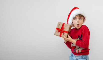 Excited funny Scandinavian caucasian child girl boy wear red Santa hat holding Christmas gift boxes dreaming over white background. Copy space. Merry Christmas presents shopping sale.