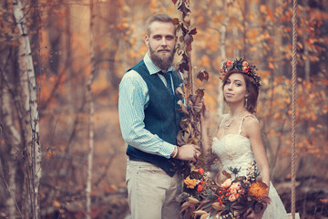 The bride and groom on a wedding walk on a decorative swing, golden autumn