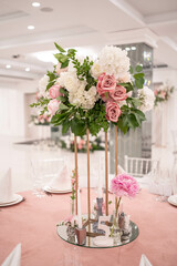 Centerpiece made of green leaves and fresh flowers stands on the dinner table. Wedding day. Fresh flowers decorations. Peony arrangements.
