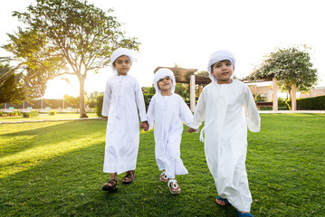Cute middle eastern kids wearing traditional arab clothing playing and having fun in a park outdoors