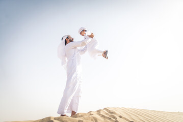 Arabian man and son wearing traditional emirates kandora dress playing in the desert