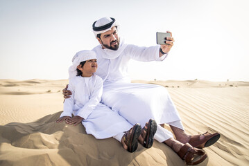 Arabian man and son wearing traditional emirates dishdasha and playing in the desert - Middle...