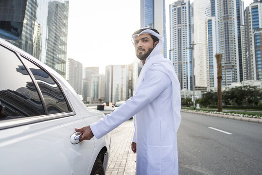 Handsome arab businessman wearing traditional emirate middle eastern clothing portrait with his luxury stretch car