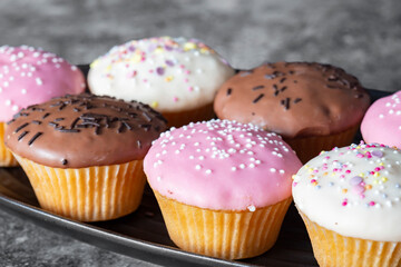 Cupcakes, decorated with icing and sprinkles on a black serving dish. On a dark concrete background