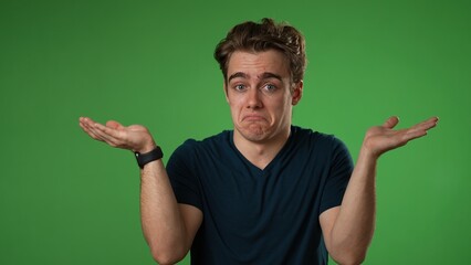 Portrait of happy young man 20s shrugging shoulders and gesturing I do not know isolated on green screen background in slow motion