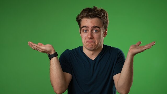 Portrait of happy young man 20s shrugging shoulders and gesturing I do not know isolated on green screen background in slow motion