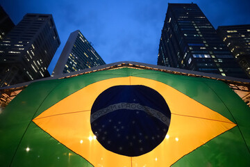 Brazilian flag at street with high buildings at night. Brazil's national symbol backlit. Patriotic...