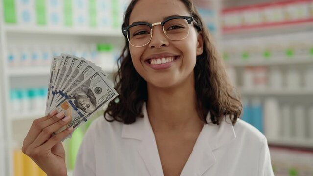 Young african american woman pharmacist smiling confident holding dollars at pharmacy