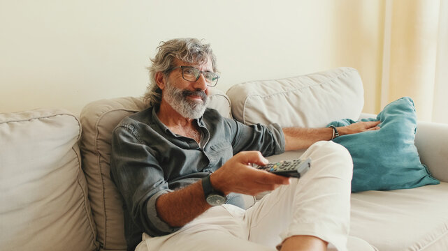 Close-up of the hand of an elderly man with remote control, changes channels while sitting on the couch at home