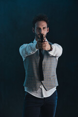 Handsome man in studio pointing gun, on dark background