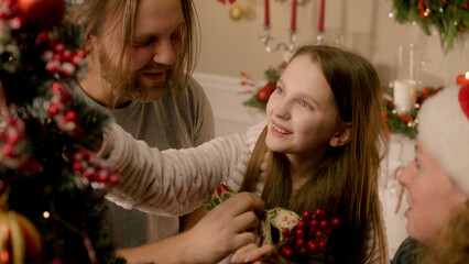 Happy caucasian family having fun and laughing. They decorating Christmas tree with balls, toys and branches at home together for Christmas or New Year. Festive decorations for winter holidays.