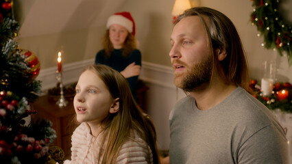 Father lift his young daughter up to put Christmas toys on tree. Happy family decorating Christmas tree and preparing home together for Christmas or New Year. Festive decorations for winter holidays.