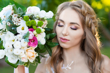 Fototapeta premium portrait of a beautiful bride who closed her eyes in a white wedding dress in the garden, close-up