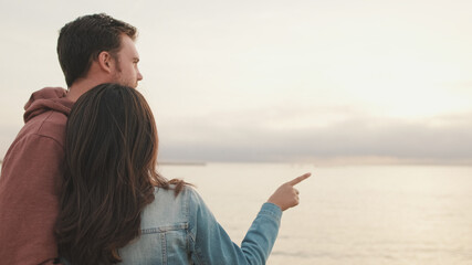 Young couple standing embracing on seascape background. Back view