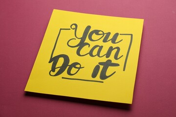 Yellow card with motivational phrase You Can Do It on burgundy background