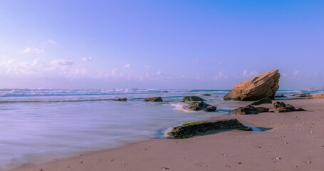 stunning view of sunset at beach with coastal rocks hit by waves. long expose effect may lead to...