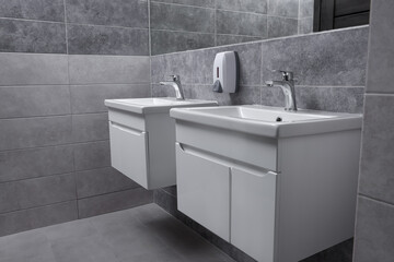 Public toilet interior with stylish white sinks and grey tiles