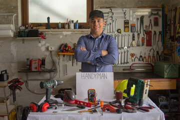 Image of a smiling man in his workshop with a bench full of work tools and the word handyman. Man...
