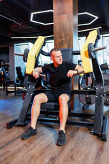 A young man in shorts and a T-shirt is sitting on an exercise machine in a gym. Healthy Lifestyle