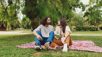 Happy smiling couple talking while sitting on blanket in park