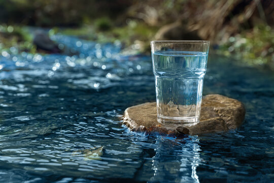 Glass of fresh water on stone near river outdoors. Space for text © New Africa