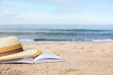 Fototapeta na wymiar Open book and hat on sandy beach near sea. Space for text