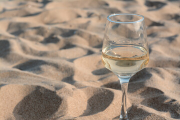 Glass of tasty wine on sand, space for text