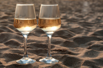 Glasses of tasty wine on sand, space for text