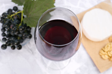 Glass of red wine and snacks served on white marble table, above view