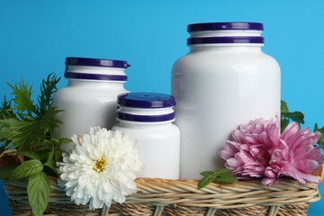 Fototapeta na wymiar White medical bottles, arugula and flowers in wicker tray on light blue background, closeup