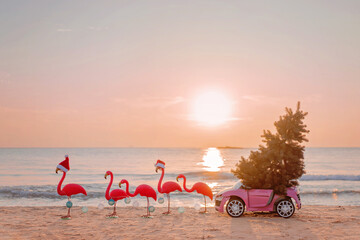 Winter flamingos are harnessed by a garland to a pink children's car with a Christmas tree in Santa...