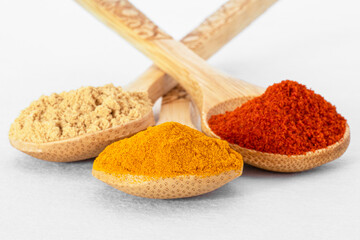 Close-up of coloured spices in wooden spoons on a white background