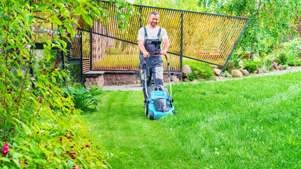 A worker mows the lawn with an electric lawn mower. The man is doing housework and at the same time...