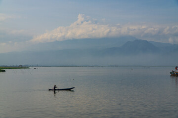 Obraz premium Traditional fishing boat looking for fish in the lake with mountains and hills in the background - Rawa Pening Lake, Semarang, Indonesia