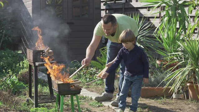 Father and son put wood pieces on barbecue grill fire
