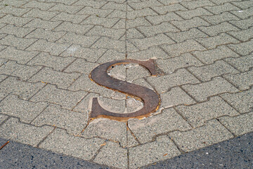 Fototapeta premium Seward, Alaska, USA - July 22, 2011: Closeup of the S letter with golden shine from South in a NWES-direction image on pavement in port