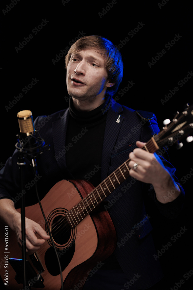 Wall mural male musician with guitar in hands playing and posing on black background in blue scenic light