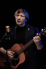Male musician with guitar in hands playing and posing on black background in blue scenic light
