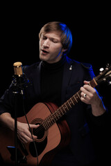 Fototapeta premium Male musician with guitar in hands playing and posing on black background in blue scenic light