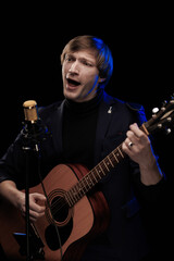 Obraz premium Male musician with guitar in hands playing and posing on black background in blue scenic light