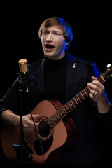 Male musician with guitar in hands playing and posing on black background in blue scenic light