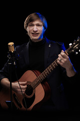 Fototapeta premium Male musician with guitar in hands playing and posing on black background in blue scenic light